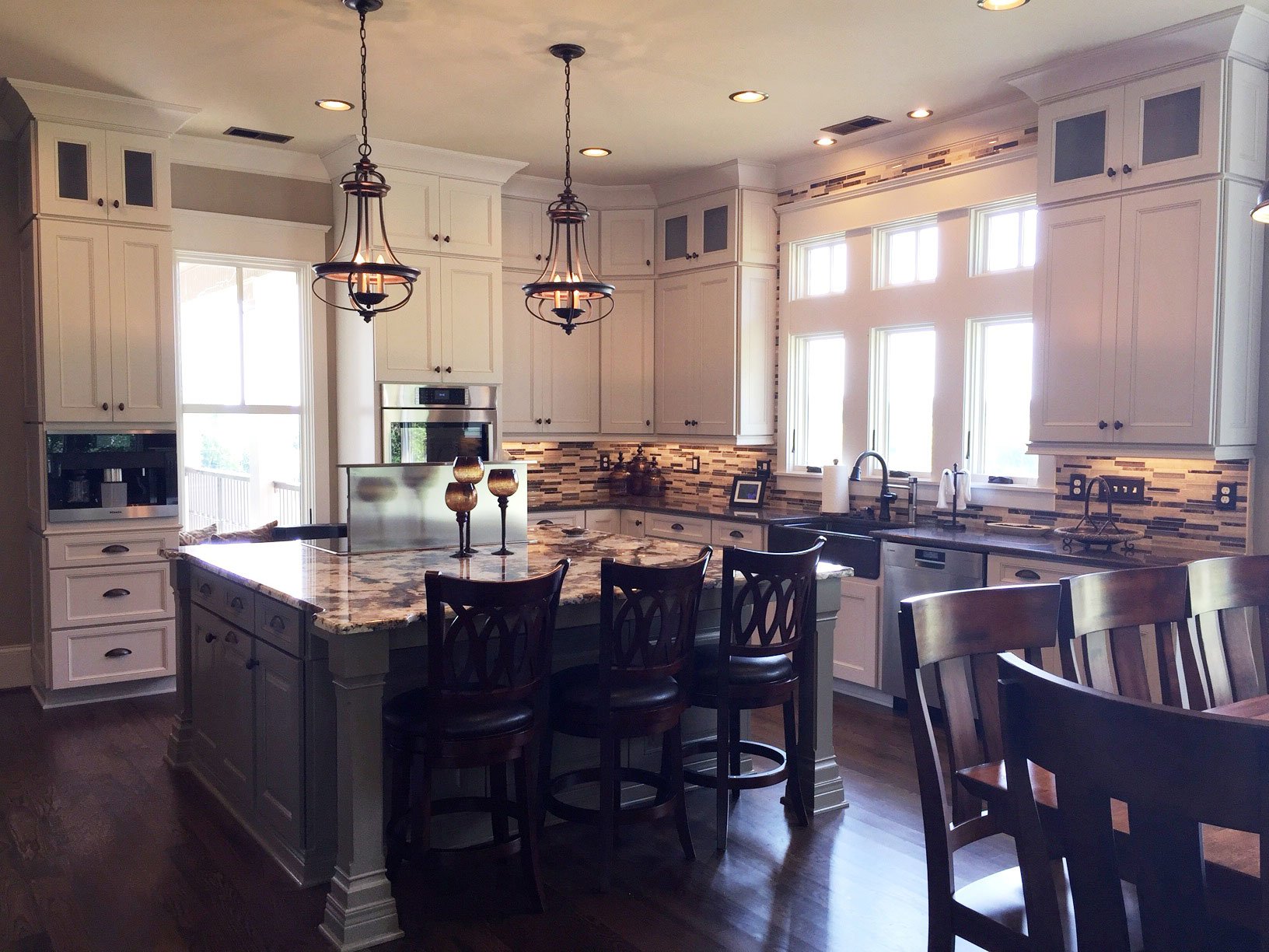 Cream painted kitchen with a grey island, granite worktops, mosaic backsplash and a farmhouse sink