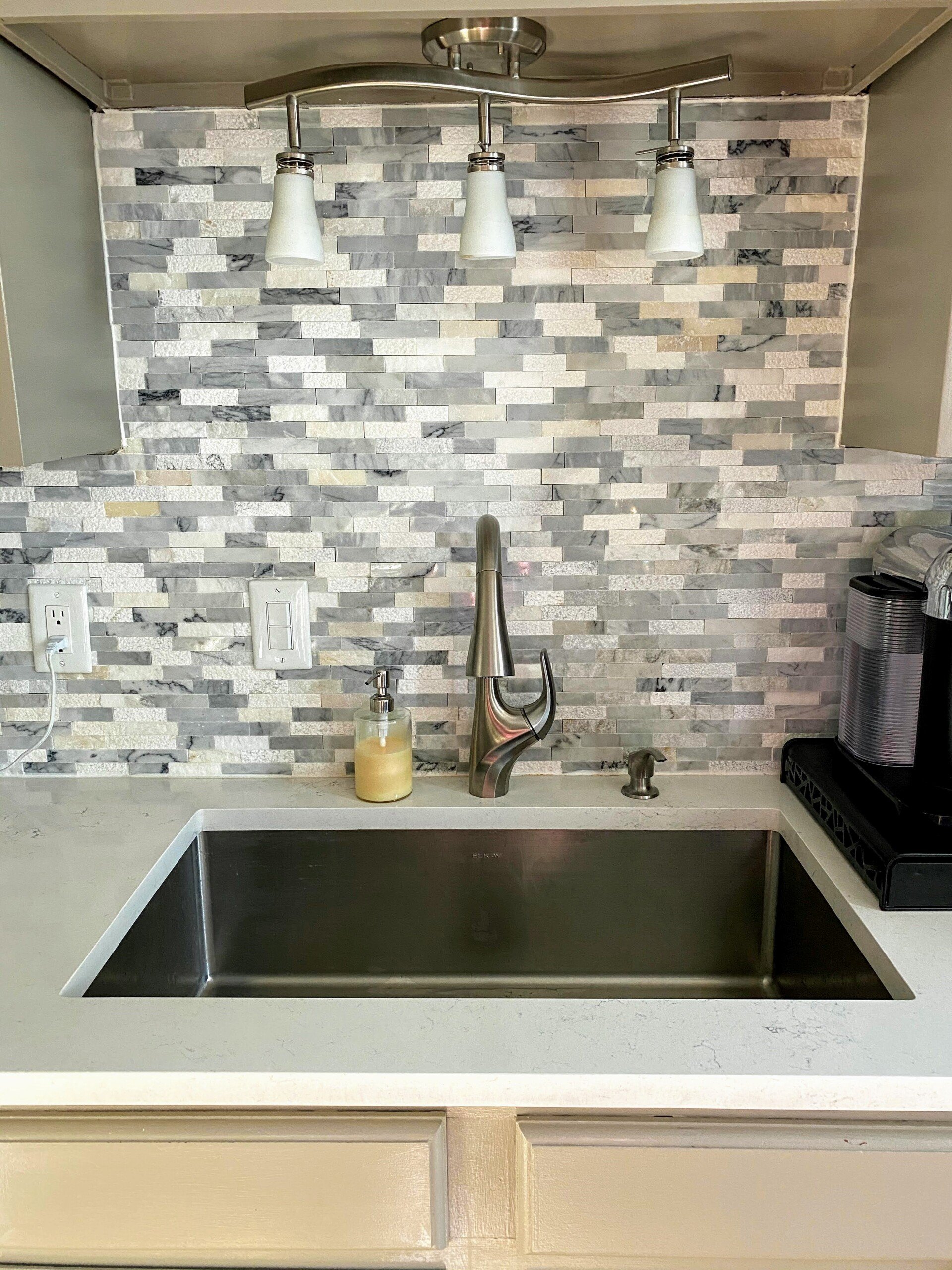 Stainless steel undermount sink set into a quartz countertop below a marble mosaic backsplash